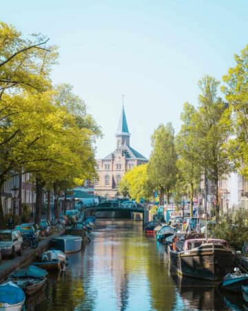 Vue d'un canal calme à Amsterdam bordé d'arbres verdoyants menant vers un clocher historique