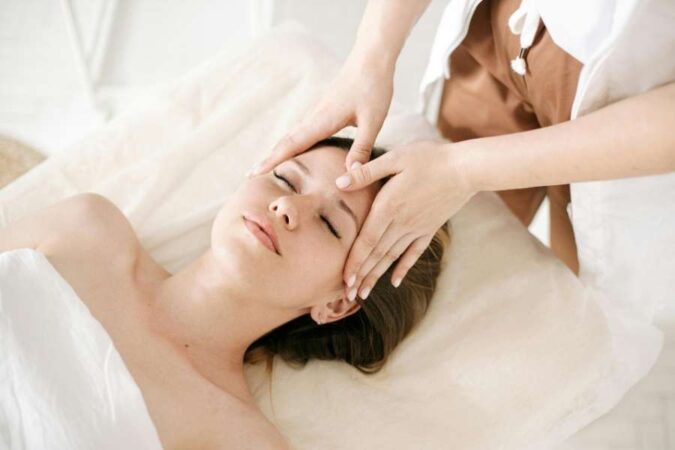 Une esthéticienne effectue des rituels de massage du visage relaxants sur une cliente allongée.