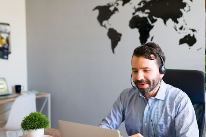 Un conseiller souriant équipé d'un micro-casque travaille sur son ordinateur portable dans un bureau moderne.